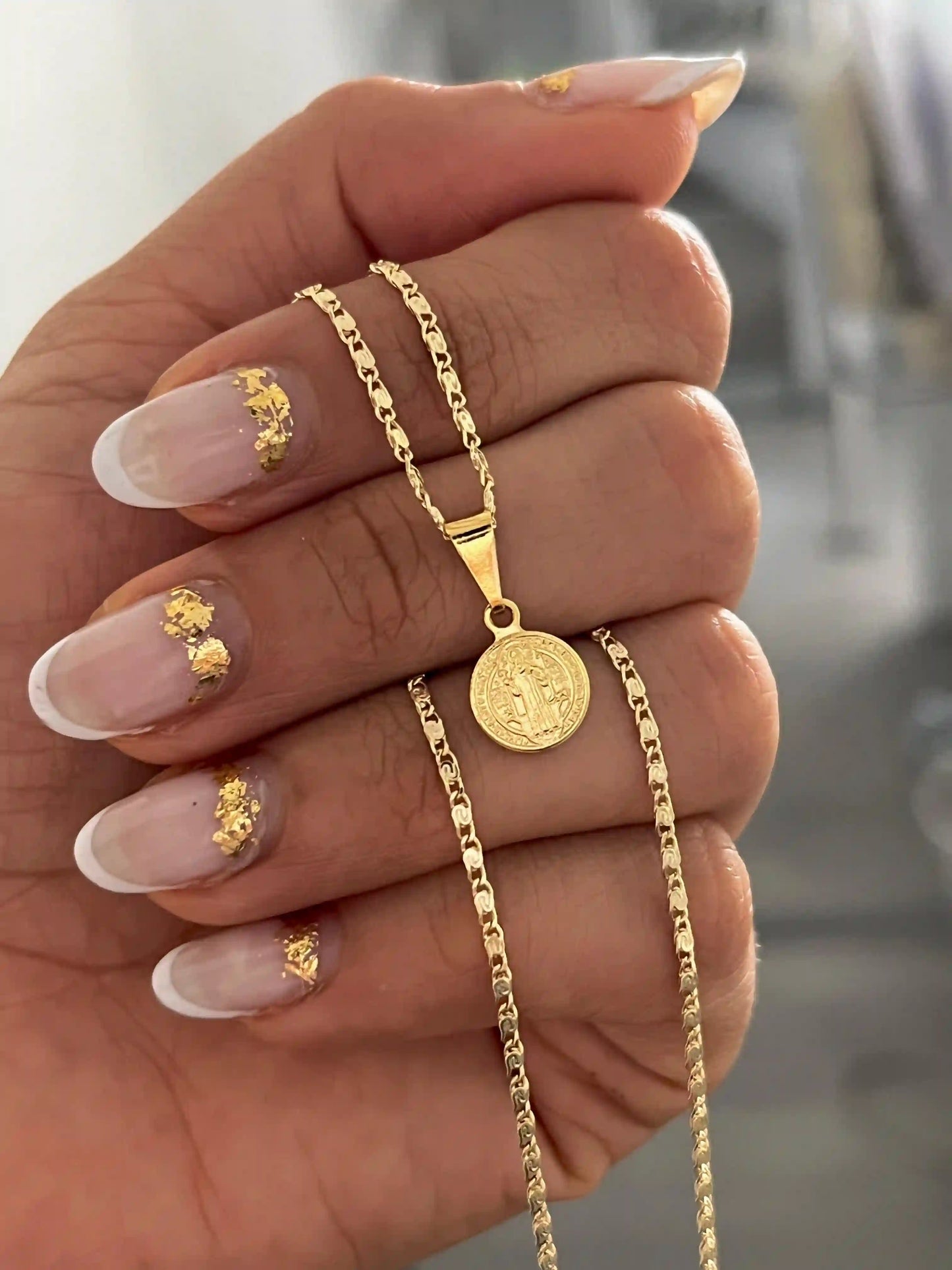 Set medalla san benito con cadena caracol 45 cm exhibida en mano de mujer en oro laminado